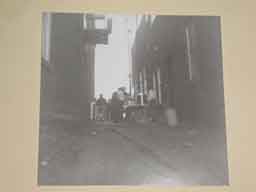 <p>A shot up the alley way that is located next to the "Amity Cemetery Ass'n" building on town square.  I would guess that the cylindrical object in the center is a coffee urn and that the people in the shot are crew lining up for chow.  Notice the electrical cables running up the alley to the square.</p>